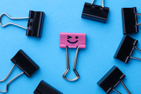 Binder clip with smiling face and faceless binders on blue background.の写真素材