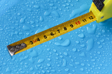 Construction tape measure on a blue background with water drops