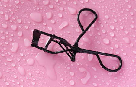 Eyelash curler on pink background with water drops