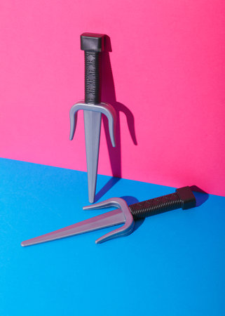 Toy plastic sai weapons on pink blue background