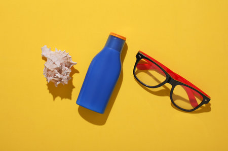Bottle of sunscreen, eyeglasses and shells on yellow background. Flat lay