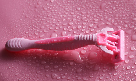 Plastic disposable razor on a pink background with water dropsの写真素材