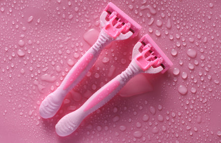 Plastic disposable razor on a pink background with water drops