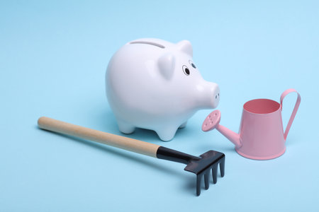 Ceramic white piggy bank with garden tools on a blue background. Business concept. Conceptual photoの写真素材