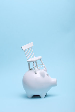 Ceramic white piggy bank with chair on a blue background. Business concept. Conceptual photoの写真素材