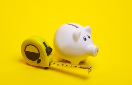 Ceramic white piggy bank with measuring tape on a yellow background.の写真素材