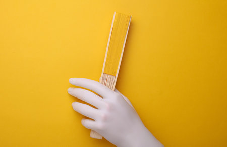 Plastic hand holding fan on yellow background.