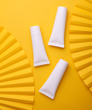 Creative top view showcase, cream tubes with fan on yellow background. Beauty concept