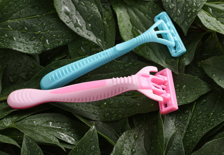 Plastic razors on green plant leaves with water drops