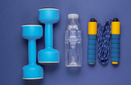 Flat lay style sport concept. Dumbbells, jump rope, bottle of water. Sports equipment on purple background. Top viewの写真素材