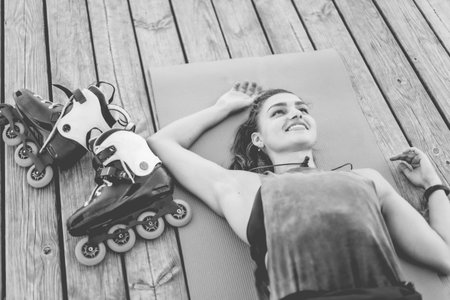 Tired but happy woman roller skater resting lying on mat outdoorsの写真素材