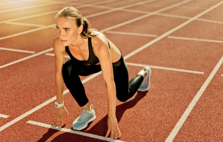 Young motivated woman runner in sportwear getting ready to run sprint at low start outdoorの写真素材