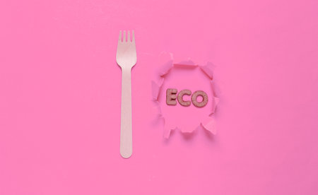 Eco-friendly wooden fork on pink background. Word eco on torn hole paper. Minimalism. Top viewの写真素材