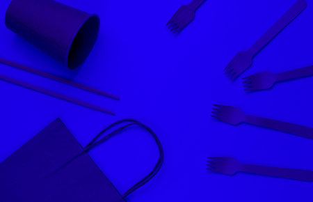 Disposable tableware of natural materials. Eco friendly concept. Wooden forks, empty craft coffee cup, bag, chopsticks. Blue light. Top viewの写真素材