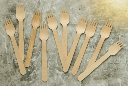 Many eco-friendly wooden forks on gray concrete background.