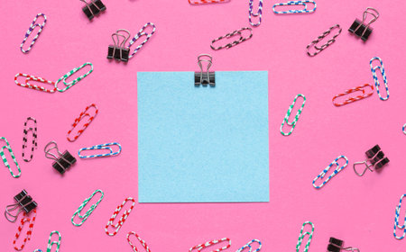 Stationery office supplies. Blue memo paper, paper clip on pink background. Top view
