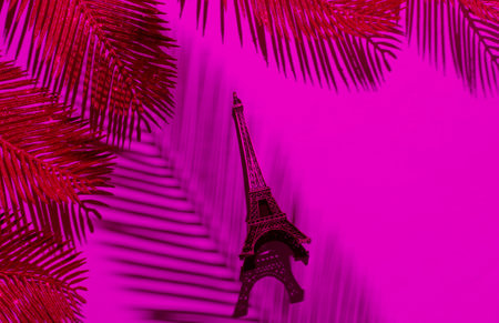 Minimalistic fashion still life. Eiffel tower figurine among decorative golden palm leaves in pink neon light. Shadow of palm leaf. Top viewの写真素材