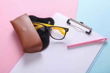 Clipboard and Leather case with eyeglasses on pink blue background. Flat lay
