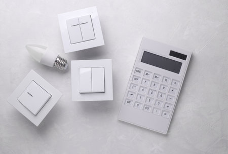 Light switches with light bulb and calculator on gray background. Electricity savingの写真素材