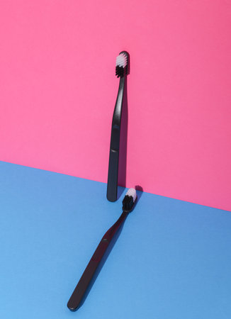 Black plastic toothbrushes on pink blue background