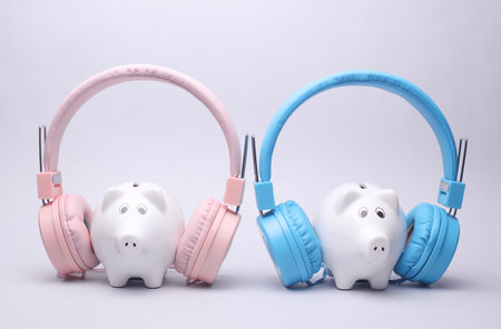 Two Ceramic Piggy Banks with Stereo Headphones on Gray Backgroundの写真素材