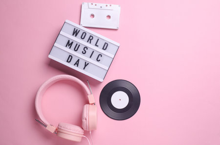 World music day text in light box and retro 80s audio cassette, stereo headphones, vinyl record on pink background. Flat lay. Top viewの写真素材