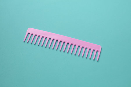 Pink plastic comb on mint green background.
