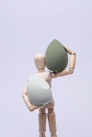 Wooden puppet holding makeup sponges on gray backgroundの写真素材