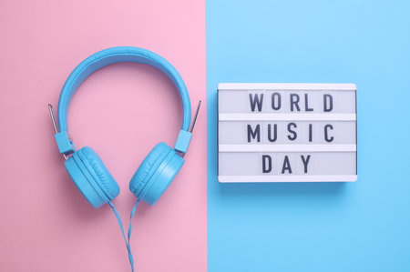 World music day text in light box and headphones on pink blue background. Flat lay