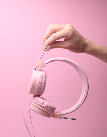 Stereo headphones in female hand on pink background