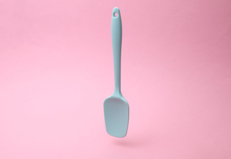 Silicone kitchen spatula floating on a pink background