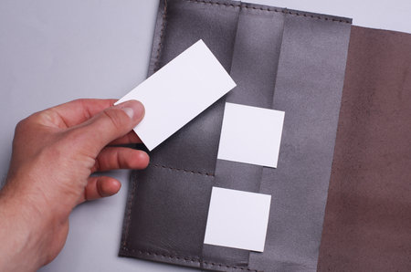 Hand taking white business card from leather business card holder on gray background