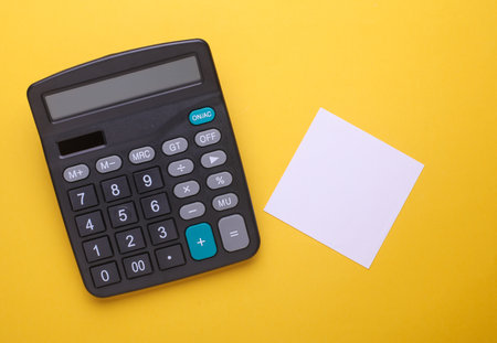 Black classic calculator with white memo paper sheet on yellow background. Top viewの写真素材