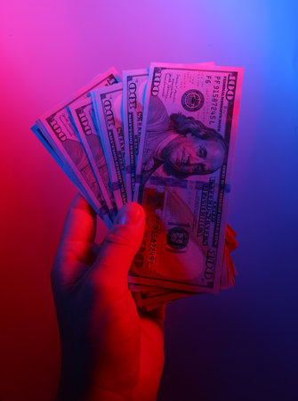 Hand holding dollar bills in red blue neon lightの写真素材