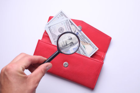 Hand with magnifying glass looks at dollars in walletの写真素材