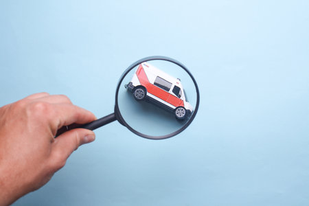 Hand looking through magnifying glass at toy ambulanceの写真素材