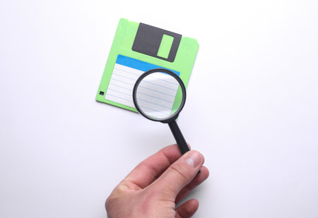 Hand with a magnifying glass examines floppy diskの写真素材