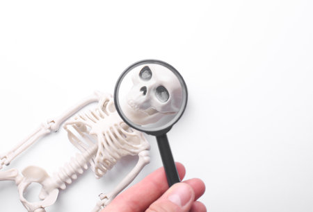 Hand with a magnifying glass examines toy skeleton