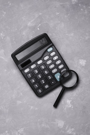 Calculator with magnifying glass on gray concrete backgroundの写真素材