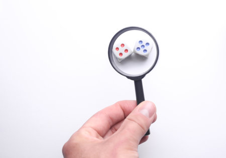 Hand with a magnifying glass examines diceの写真素材