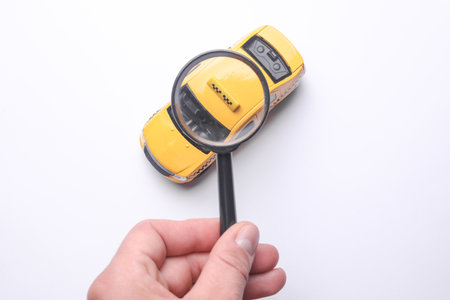 Hand with a magnifying glass examines toy taxi carの写真素材