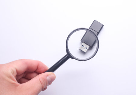 Hand with a magnifying glass examines usb memory stick