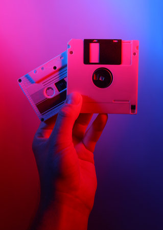 Hand holding Retro floppy disk and audio cassette in red blue neon lightの写真素材