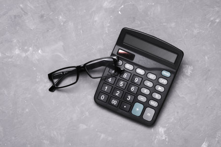 Black classic calculator with eyeglasses on gray concrete backgroundの写真素材