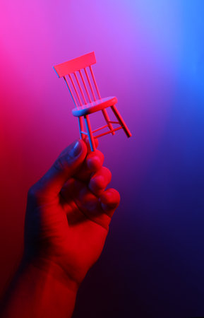 Hand holding chair miniature in red blue neon lightの写真素材