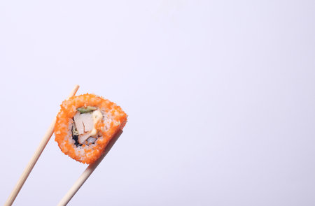 Chopsticks holding sushi roll on white backgroundの写真素材