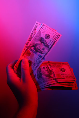 Hand holding dollar bills in red blue neon lightの写真素材