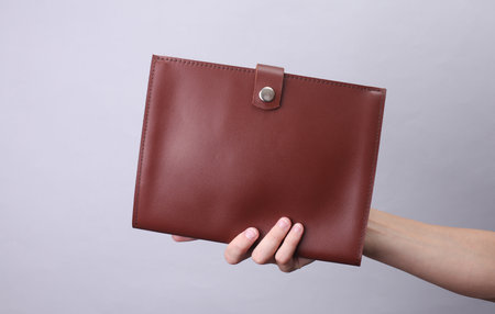 Hand holding brown leather document organizer folder on gray background