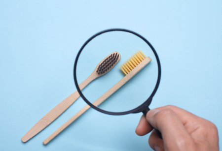 Hand with a magnifying glass examines bamboo toothbrushes on blue backgroundの写真素材