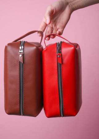 Female hand holding leather cosmetic bags on pink background